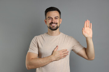 Man making promise with raised hand on grey background. Oath gesture