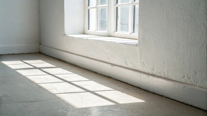 Closeup of a white wall the surface clean and unblemished with a faint shadow of the window frame tracing a perfect rectangle of light onto the floor.