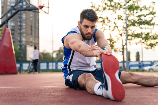 Muscular Athlete Warming Up With Stretches On Basketball Training Court