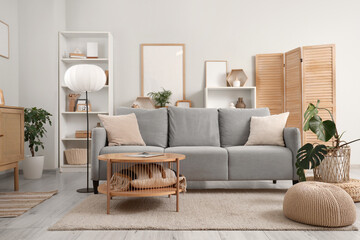 Interior of light living room with grey sofa, lamp and plants