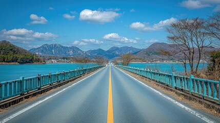 Obraz premium A serene road stretches toward mountains and water under a clear blue sky.