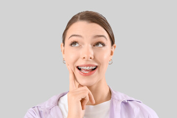 Thoughtful young woman with dental braces on light background, closeup