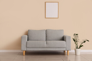 Stylish grey sofa, blank photo frame and houseplant near beige wall