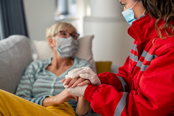 Female emergency responder in red uniform monitors vital signs of elderly Caucasian patient wearing...