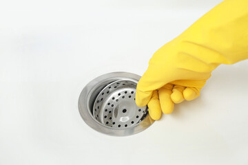 Female hand in rubber glove placing drain strainer in ceramic kitchen sink, closeup
