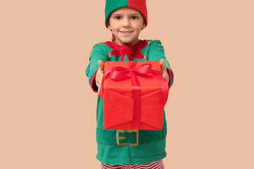 Cute little girl in elf costume with Christmas gift box on beige background