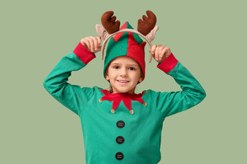 Cute little girl in elf costume with Christmas headband on green background