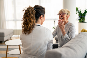 Obraz premium Caucasian female physician in white coat conducts friendly medical consultation with senior patient during residential healthcare visit, sharing positive interaction.