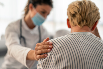 Fototapeta premium Female Caucasian doctor in white coat and medical mask provides compassionate care to senior Caucasian patient during professional home healthcare consultation.