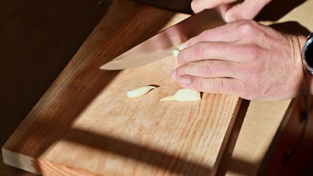 Man chopping garlic on a wooden board in a home kitchen