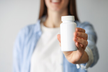 Woman holding medical bottle with pills on light background, closeup
