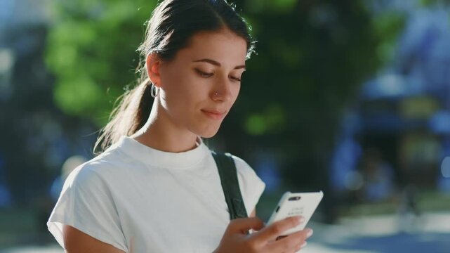 Focused Young Hispanic Teen Woman Using Smartphone in Sunlit Urban Setting