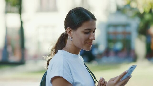 Smiling Hispanic Young Woman Using Smartphone Outdoors