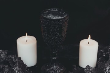 A gothic depiction of an ornate black goblet filled with water, surrounded by dim candlelight and dark, moody shadows