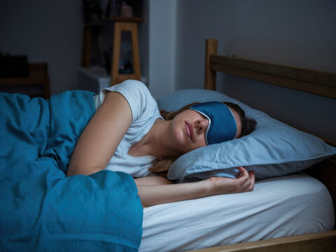 mujer que lleva una m&aacute;scara para los ojos y duerme en una cama en casa. La mujer est&aacute; acostada de lado, con la m&aacute;scara que le cubre los ojos
