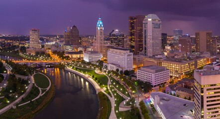 Fototapeta premium Evening cityscape of downtown Columbus, Ohio. Illuminated buildings and parkland along the Scioto River. Aerial view. DOWNTOWN, COLUMBUS, OHIO, UNITED STATES