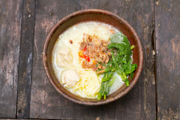 Noodle soup with vegetables, meatballs, and fried shallots, served in a clay bowl placed on a dark...