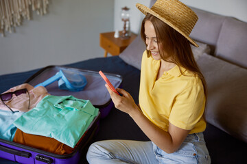 Happy young woman chatting with friends via smartphone before travelling