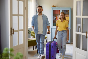 Young man and woman couple leaving home with packed travel suitcase