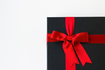A black gift box with red ribbon on white surface with copy space
