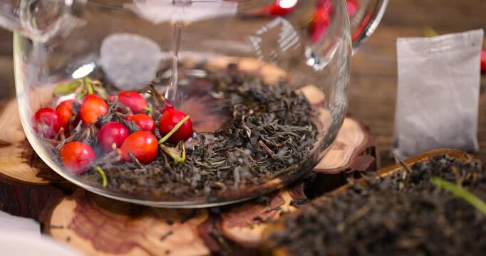 teapot with brewed tea with rose fruits, red rosehip fruits and hot green tea in a transparent teapot