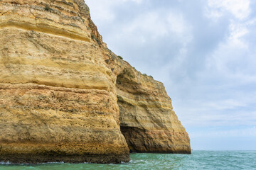 At dusk, Golden coastal cliffs rising above emerald waters with intricate sea caves. Features...