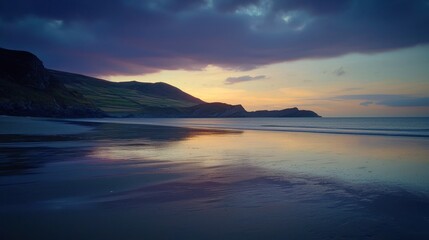 Obraz premium Serene sunset over tranquil beach with hills and calm ocean reflecting colors.