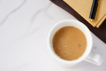 ミルクをたっぷり入れたコーヒー、カフェ・ラッテを飲みながら、茶色の革のシステム手帳でデスクワークをしているイメージ
