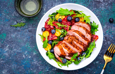 Foodie food salad with grilled duck and citrus, berries and lettuce on blue background, top view