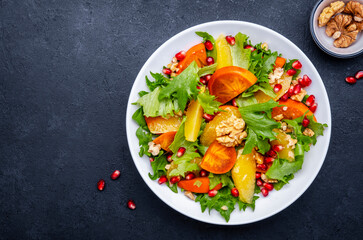 Winter vegan  persimmon salad with pomegranate, walnuts, oranges and lettuce, black background, top...