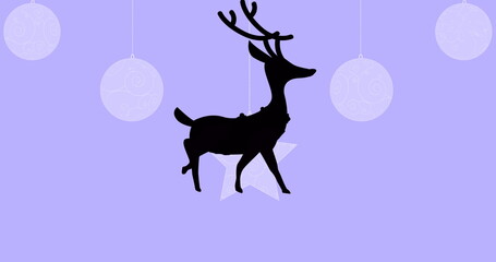 Black silhouette of reindeer walking over christmas hanging decorations against purple background
