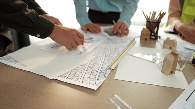 Smart architect and safety engineer discussion about building blueprint on table with architectural document, measurement tools and wooden block scatter around at modern office. Closeup. Delineation.