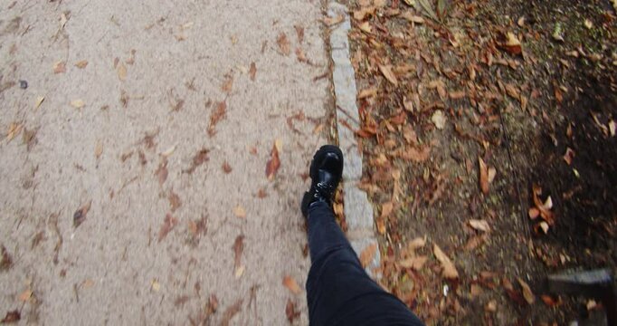 Beautiful slow motion shot in a subjective shot as we see a man's legs walking through a park with dry leaves lying around.
