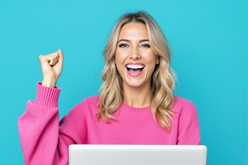 Naklejka premium Smiling woman with raised fist in excitement, wearing a pink sweater, sitting at a laptop, on a turquoise background. Concept of success and achievement. Ai generative