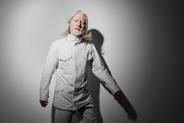 Portrait of an elderly man with long white hair in a white outfit against a grey background, conveying a sense of introspection and elegance His expression is thoughtful and serene