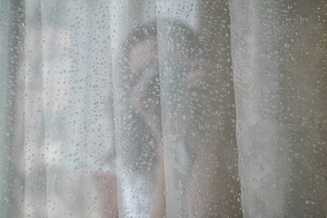 Window glass covered with raindrops and the silhouette of a girl reflected in it