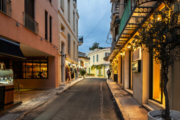 A narrow street of gift and souvenir shops and cafes in the colorful illuminated Plaka district at night in Athens, Greece.	