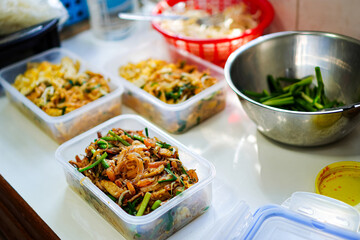Side view of Pad Thai with fresh squid and prawns and vegetarian Pad Thai in lunch boxes arranged on kitchen table in home kitchen.