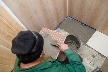 A man is laying tiles in a bathroom