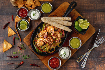 Shrimp fajitas on wooden table with sauces and tortillas on the side