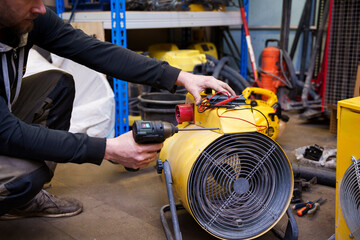 male repairman fixing industrial air heater in workshop