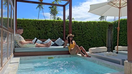 Working remotely in a tropical paradise, a freelancer enjoys a serene poolside setting, A diverse couple of man and woman at a pool villa, a freelancer at work by the pool - Powered by Adobe