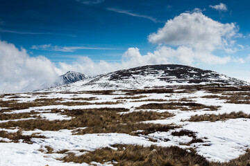 Winter spring mountain landscape changing season heather vast plains highest mountain in the Czech Republic - Sněžka covered in snow, dramatic clouds in strong wind on a sunny day
