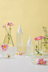 Advertising photo for skincare products. In front of two dropper bottles set in the middle of a glass podium, nearby laboratory glassware containing chamomile branches, positioned on a yellow backdrop
