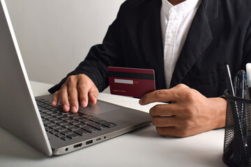 Hand holding credit card and using laptop. Businessman or entrepreneur working from home. Online shopping, e-commerce, internet banking, payment, spending money, work from home concept.