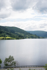 Norwegian Natural Landscape with Mountains with Green Trees Growing Next to a Lake with an Asphalt Road Running Along It.