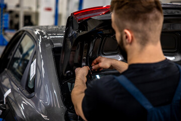 experienced auto mechanic repairs car wiring in trunk at auto repair shop