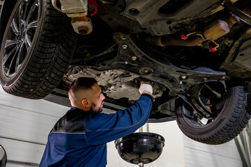 A working car mechanic unscrews the drain plug of the crankcase on the pallet to drain and replace...