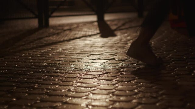 Female feet walking on wet sidewalk after rain at night, car passing on street. Low POV
