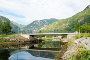 concrete bridge over a river with water like a mirror reflecting the beautiful Norwegian fjord mountains in the village of L&aelig;rdals&oslash;yri.